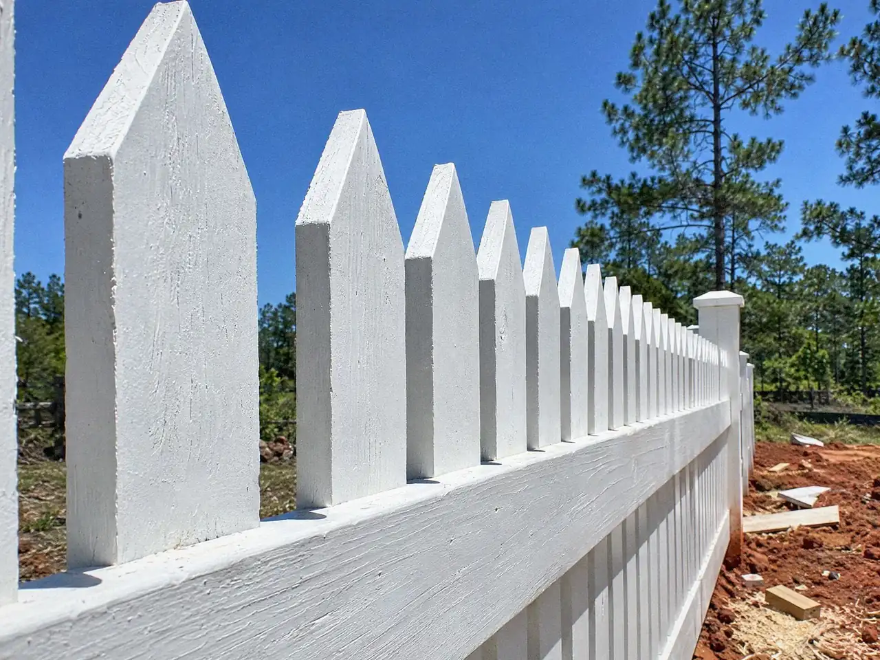 Low-angle close-up of pointed white picket tops against a blue sky