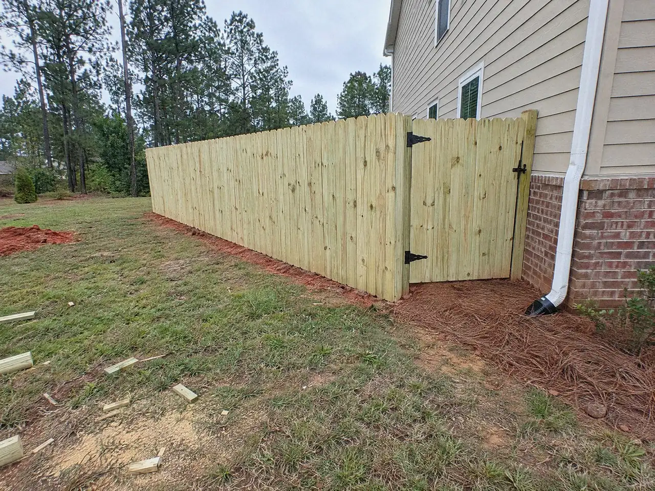 Six-foot wood privacy fence meeting the back corner of a house, with a matching walk gate on black hinges